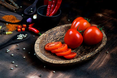 red chili and tomato, salt, garlic, rosemary on a dark wooden background; ingredients for cooking;...
