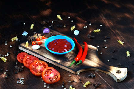 red chili and tomato, salt, garlic, rosemary on a dark wooden background; ingredients for cooking; cover cookbook; asian cuisine, free space for textの写真素材