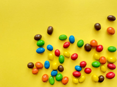 Assorted colorful candies scattered on a vibrant yellow background - perfect for joyful and playful...