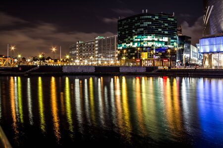 Modern illuminated business offices at night. Long reflections on the river from the lit windows and street lights. Tranquil water reflecting lights on its surface.の写真素材