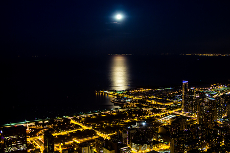 Night city lights with moonlight on the lake. Dark night skyline, city lights fill all the streets and highways, moonlight runs from the far horizon to the very city on the flat and soft lake surface.の写真素材