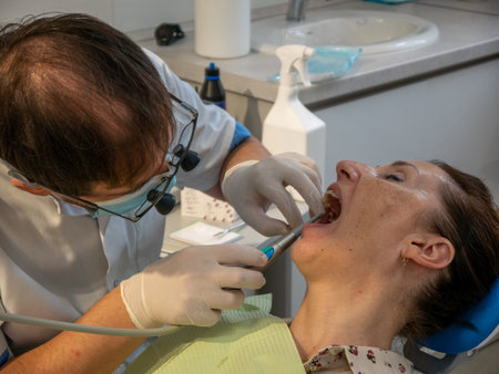 The patient is in the dental chair with her mouth open while the dentist treats her teeth.の写真素材