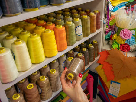 Shelves with threads of various colors. Close-up female hand choosing threads for sewing her future...