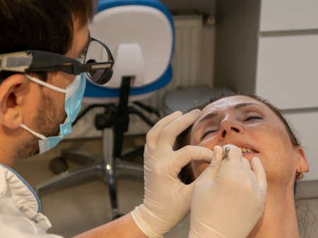 The female patient is in the dental chair with her mouth open, while the dentist treats her teeth.の写真素材