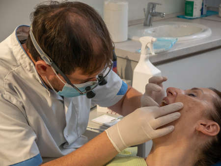 Dentist's office. The patient lies in the dental chair with her mouth open, while the dentist tries on a new denture tooth.の写真素材