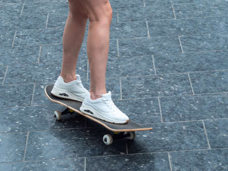 Close-up of female legs in white sneakers on a longboard. Skateboard with girl legs. Youth leisure concept.の写真素材