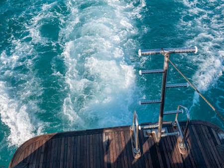 An iron ladder at the stern of the boat against the backdrop of a foaming trail on the water behind the boat.の写真素材