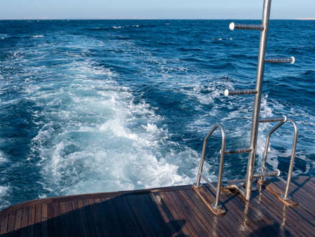 An iron ladder at the stern of the boat against the backdrop of a foaming trail on the water behind the boat.の写真素材