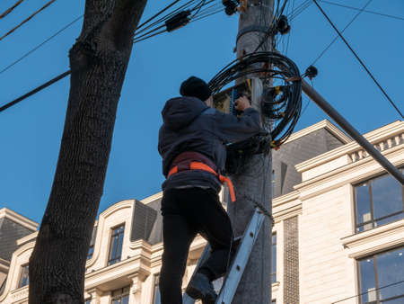 An electrician on a ladder installs a junction box for the Internet on a pole.の写真素材