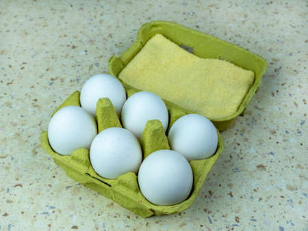 Six white chicken eggs in a green egg box, close-up.