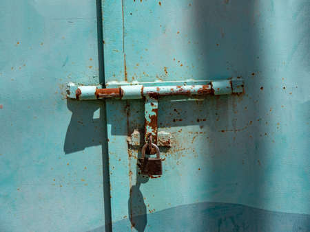 Close-up of a blue metal massive door with an iron bolt and padlock.