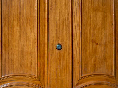 Door peephole on a wooden front door with a beautiful texture.