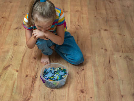 A little girl on a wooden floor enthusiastically collects puzzles.の写真素材