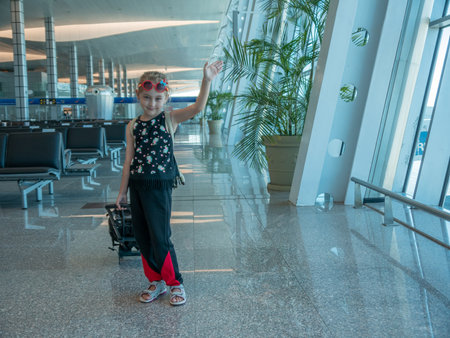 Smiling little girl tourist at the airport waving goodbye. Smiling little girl cheerfully waves goodbye at the airport.の写真素材
