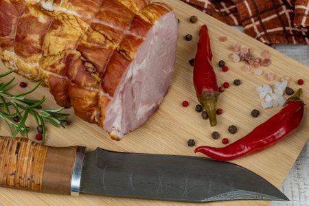 Traditional ham on a wooden cutting board with a carving knife, colorful allspice, red hot peppers,...