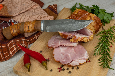 Traditional ham sliced on a wooden cutting board with a carving knife, multi-colored allspice, red hot peppers, parsley, dill and basil. The concept of snacks from pork meatの写真素材
