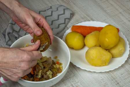 Peeling boiled potatoes. The female hand with an iron table knife removes the peel from the boiled yellow potatoes, puts the peeled potatoes on a plate. Close-up from the top sideの写真素材