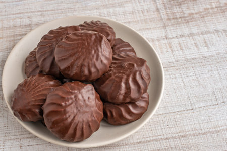 A close-up heap of chocolate marshmallows lying on a white glass plate. The concept of the negative...