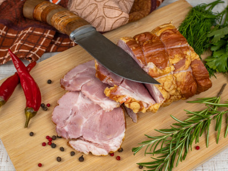 Traditional ham sliced on a wooden cutting board with a carving knife, multi-colored allspice, red hot peppers, parsley, dill and basil. The concept of snacks from pork meatの写真素材