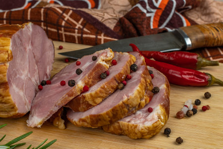 Piece of juicy and tasty bacon cut into delicious slices on a wooden cutting board with a carving knife, multi-colored allspice peas, red hot peppers, parsley, dill and basil. Concept of cooking meatの写真素材