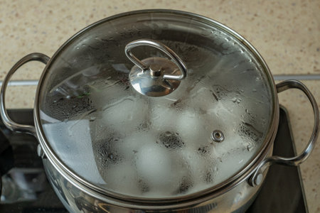 Iron pan with boiling water in which white chicken eggs are boiled. Water boils and boils in pan...