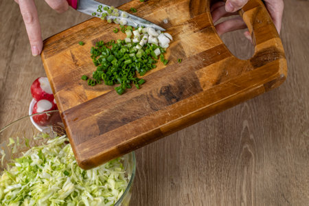 The female prepares a salad of fresh vegetables. Close-up of a wooden cutting board with chopped green onions poured into a salad bowl. Healthy lifestyle. The concept of healthy vegan raw foodの写真素材