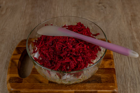 Housewife stirs a fresh vegetable salad with a plastic spatula in a glass bowl. Close-up of a female hand stirring salad with a plastic spoon in a glass salad bowl. Concept of veganism and raw foodの写真素材