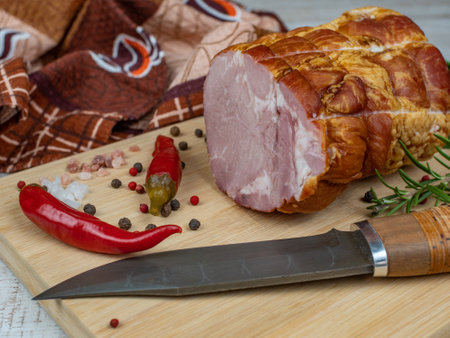 Traditional ham on a wooden cutting board with a carving knife, colorful allspice, red hot peppers, parsley, dill and basil. The concept of delicious meat snacks from pork meatの写真素材
