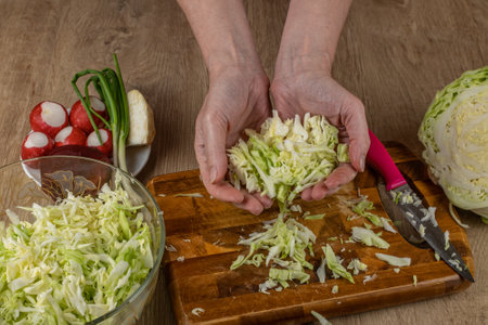 The female prepares a vegetable salad. Close-up female hands putting chopped white cabbage into a bowl with vegetable salad. The concept of cooking fresh vegan healthy saladsの写真素材