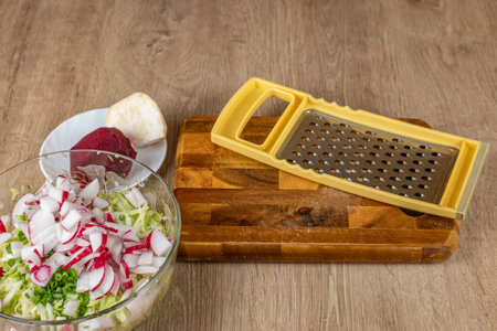 Preparation of vegetable salad from fresh vegetables. Vegetable iron grater on a wooden cutting board and a bowl with chopped and grated vegetables. The concept of cooking fresh vegetable saladの写真素材