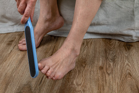 A woman rubs her heels with a double-sided foot grater. The female cleans her feet with a grater, removing calluses from her heels. Pedicure tool. Foot care. Womens health conceptの写真素材