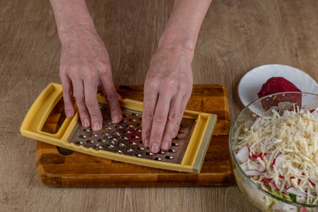 A housewife rubs red beets on an iron grater. Close-up of female hands rubbing red beets on a vegetable grater for a vegetable salad. The concept of veganism and raw foodの写真素材