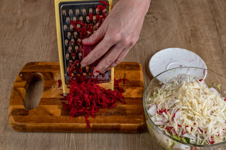 A housewife rubs red beets on an iron grater. Close-up of female hands rubbing red beets on a vegetable grater for a vegetable salad. The concept of veganism and raw foodの写真素材