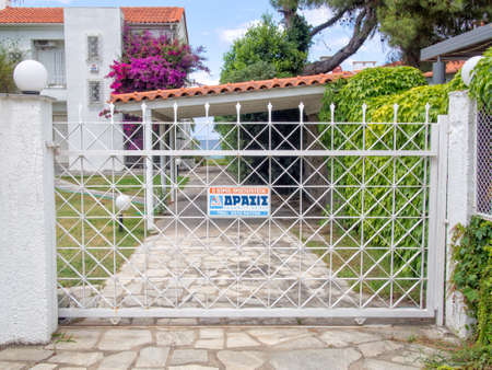 POLYCHRONO,GREECE -JUNE 02 2014 : Security gates used to protect the entrance to a house with a warning sign from the security firm protecting it.のeditorial素材