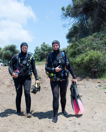 AVLAKI,GREECE-JULY 04 2015 :Two female Scuba Divers walk to the sea with their equipment to go for a dive..Diving is an adventurous sport with dive sites in most countries around the world.のeditorial素材