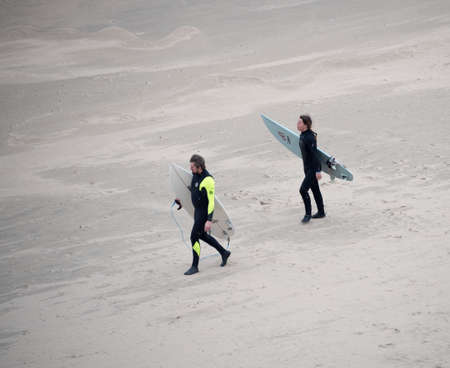WALES - UK , OCTOBER 22 2015 : Two surfers carrying their boards walk down a beach to the sea to go surfingのeditorial素材