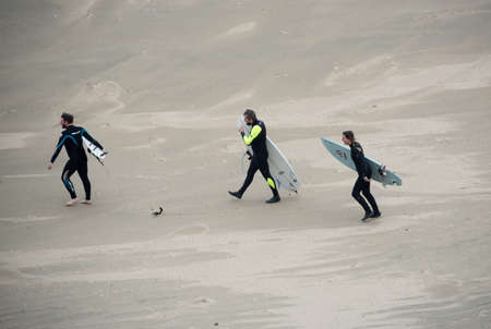 Wales - UK , October 22 2015 : Three surfers carrying their boards walk down a beach to the sea to go surfing.のeditorial素材