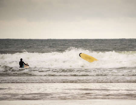 Surfer on a cold day in the Autumn has a wipe out and falls into the sea.の写真素材