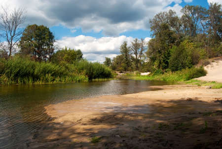 A small river, with a background of blue sky and green forestの写真素材