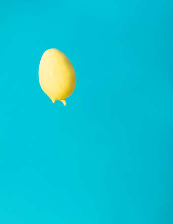 An egg hovering in the air covered with yellow paint on a blue background. Easter concept. Complementary colors.の写真素材