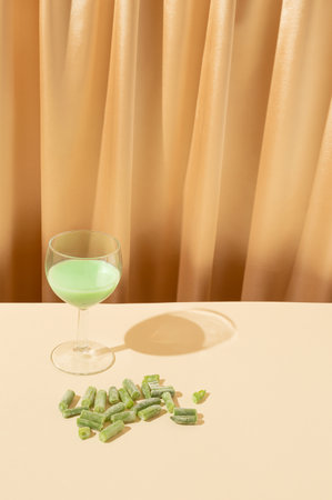 A glass of green drink and a bean next to it on a beige curtain background. Healthy food concept 2021の写真素材