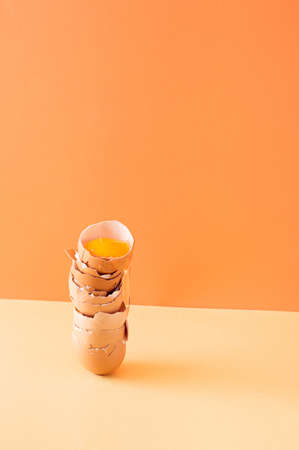 Egg shells arranged one on top of the other and a raw egg leaking from the top. Light orange and cream  background. Easter 2021 concept. Pastel colors.の写真素材