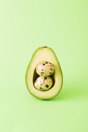 Avocado containing two quail eggs ona a green background. Easter creative concept 2021. Minimal photography style.の写真素材