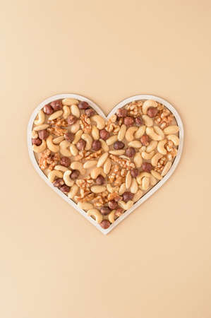 Mixed nuts: walnut, hazelnut, cashew and almond arranged in a white heart frame on a cream background. Healthy food vegetarian life style keto concept. Flat lay photography.の写真素材