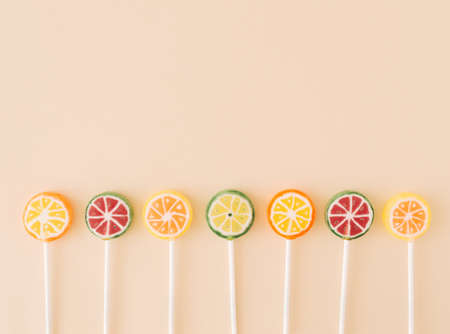 Seven lollipops that face watermelons, oranges, lemons and limes on a cream background. Candy food minimal summer concept with copy space aboveの写真素材