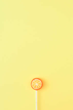 Sweet orange lollipop on a yellow background with a large copy space. Minimal summer candy concept. Monochromatic colorsの写真素材