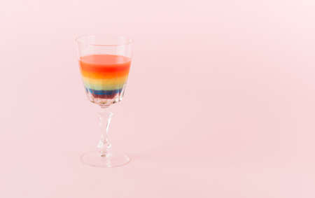 A rainbow cold cocktail drink on a pink background. Rainbow colors precisely arranged in the glass. Party summer concept with a large copy space.の写真素材