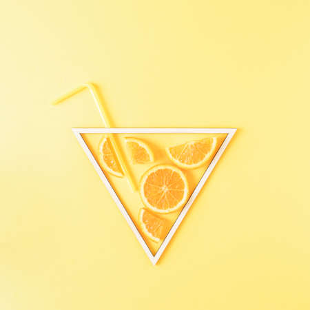 White triangle frame filled with pieces of orange and straw on a yellow background. Surreal glass of...