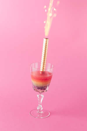 Cocktail drink rainbow color in which fireworks are placed on a pink background. Ice and fire. Party and celebration conceptの写真素材