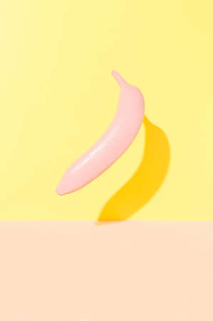 Painted in pink flying banana fruit on a combination of yellow and pink background. Fruit summer conceptの写真素材